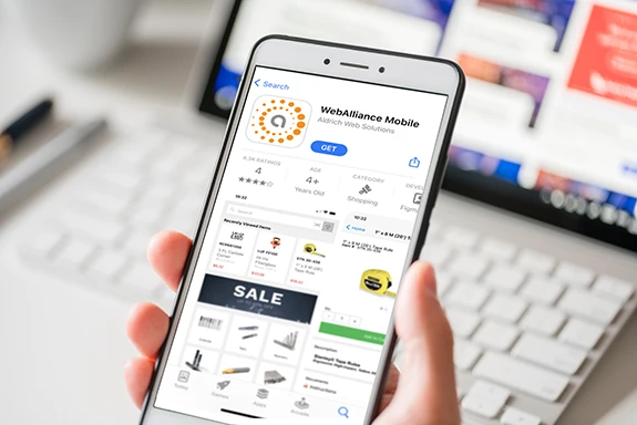 Photo of a person holding a phone using the Aldrich Solutions WebAlliance Ecommerce Mobile App in soft focus